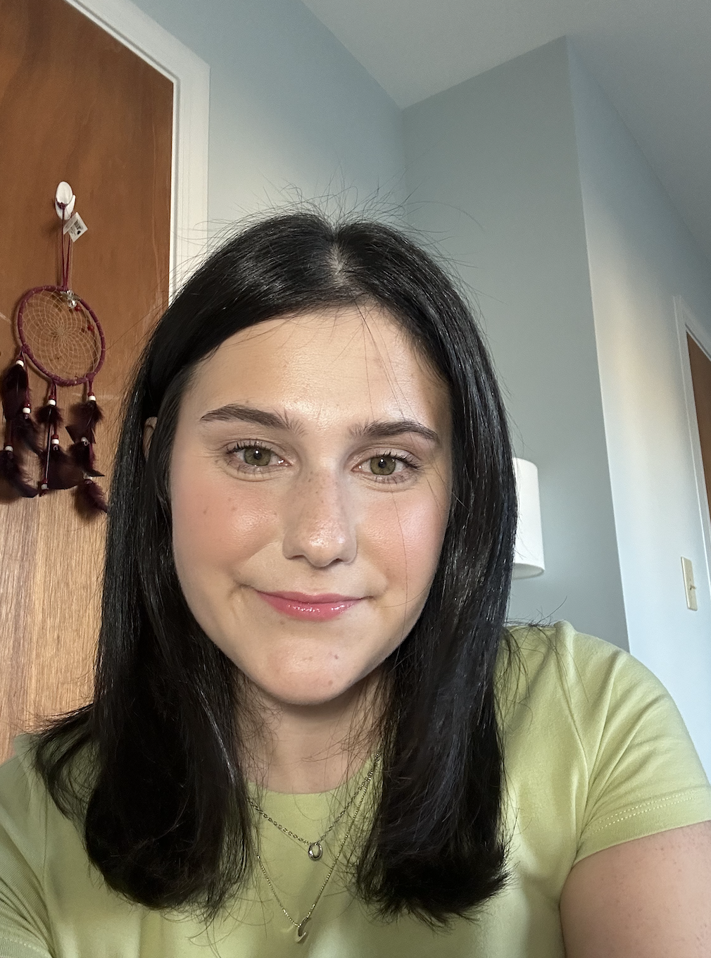 A colored rectangular portrait of Caitlin. She has on a green shirt. Her hair is dark brown and straight. There is a blue wall behind her.